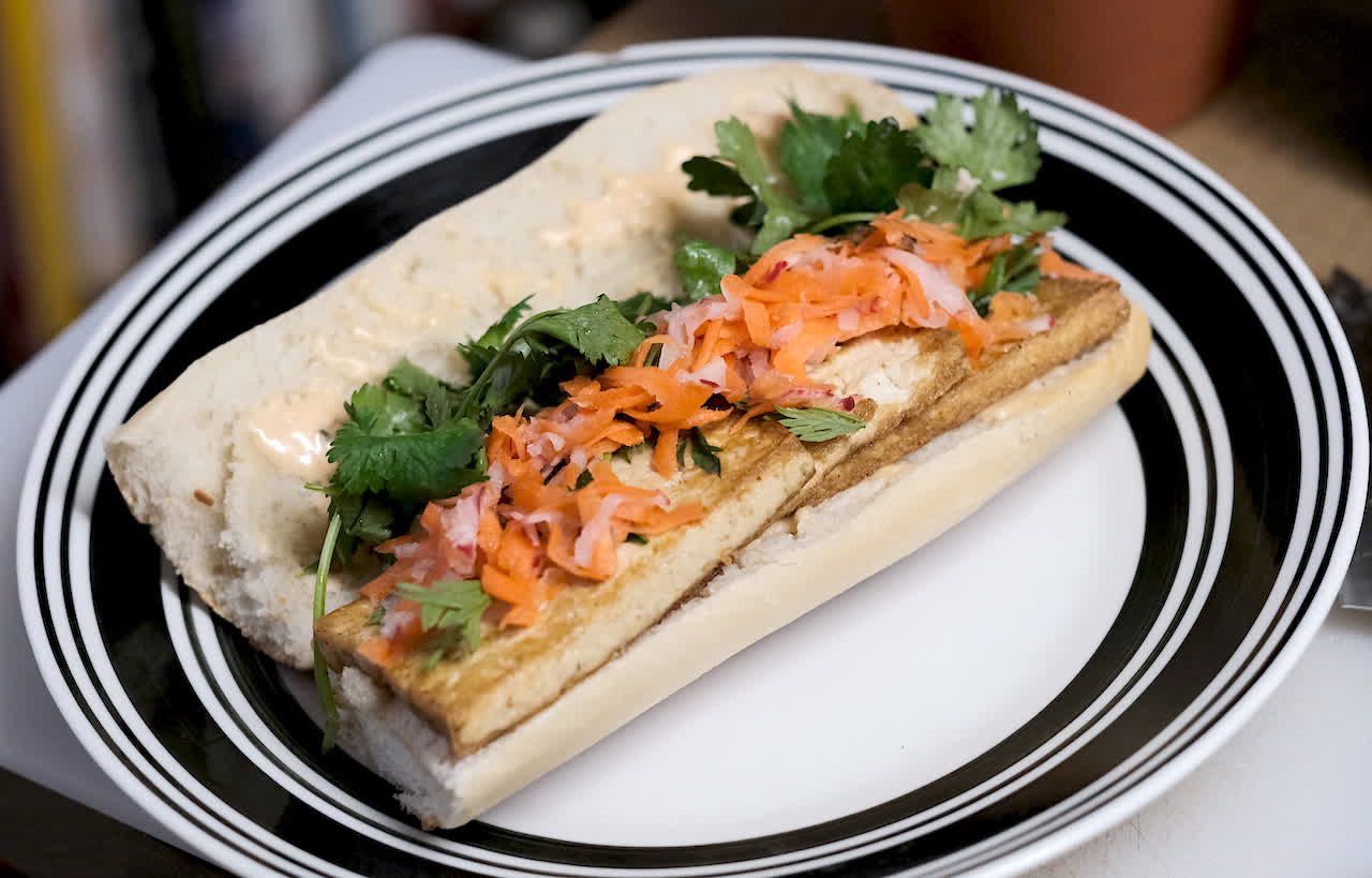 Tofu banh mi on a plate, topped with carrot and radish pickles and cilantro.
